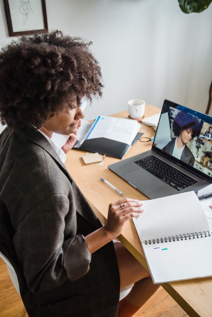 Businesswoman engaged in video conference, taking notes at desk.