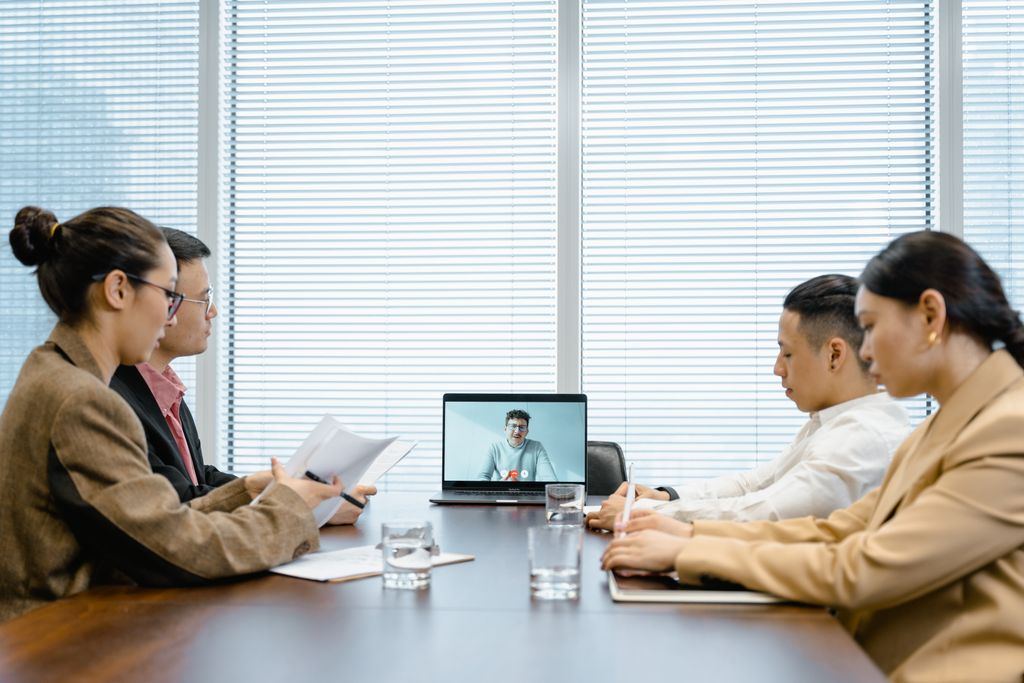 Four colleagues in a conference room engaged in a meeting with remote participant on video call.