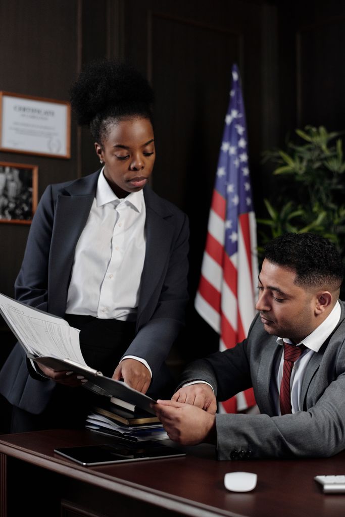 Two professionals reviewing documents in an office with an American flag in the background.